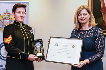 Sgt. Danielle Thacker holding an apprenticeship award certificate at a formal presentation event.<br />
